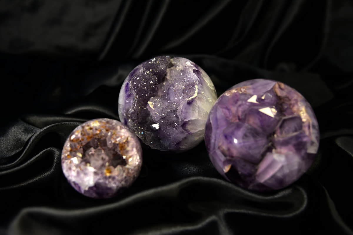 Three polished amethyst spheres in graded sizes on black fabric, a repeatable line retailers buy wholesale among other crystals