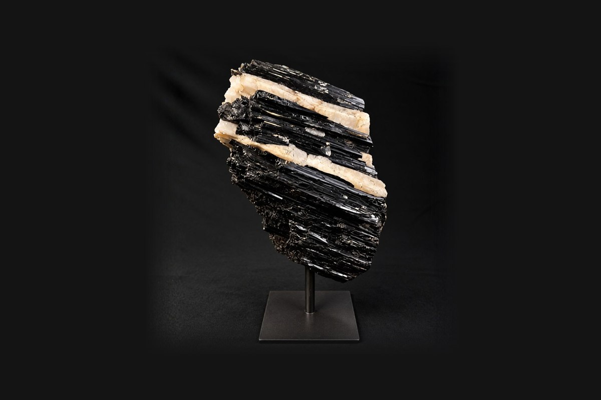 A black tourmaline specimen with white quartz bands on a metal stand