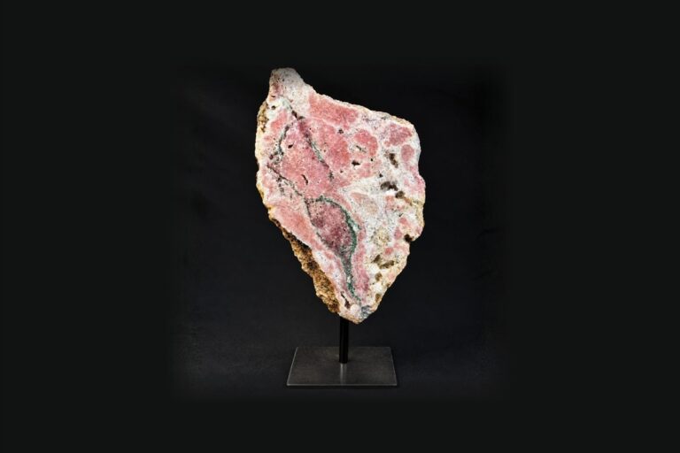 A pink mineral slab mounted on a metal stand against a black background