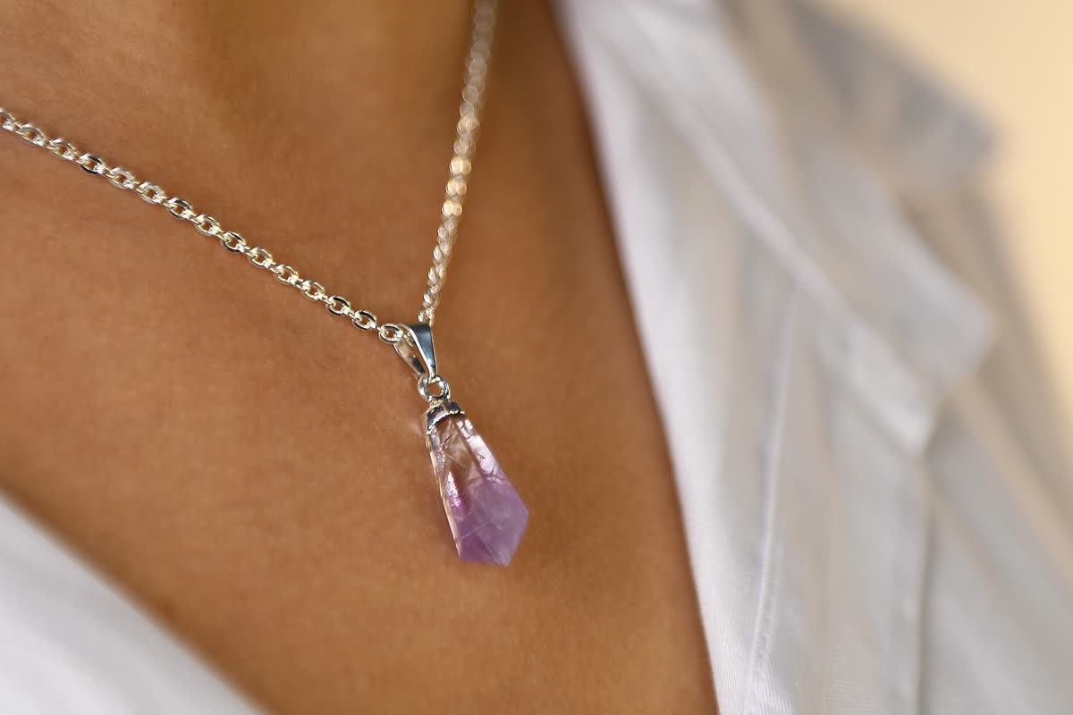 A faceted pale amethyst pendant on a fine silver chain, worn at the collarbone over a white shirt