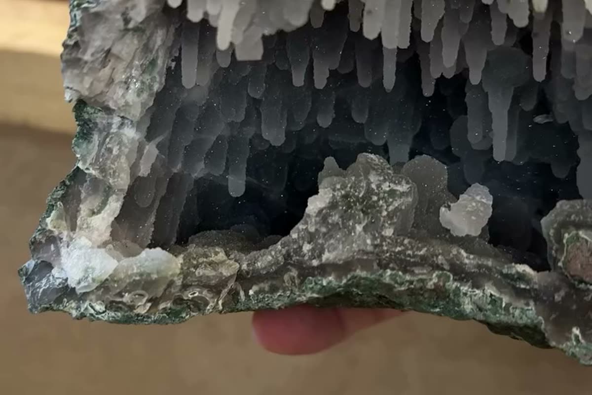 A chalcedony stalactite formation inside a cut Brazilian geode, showing concentric banding around the central tube