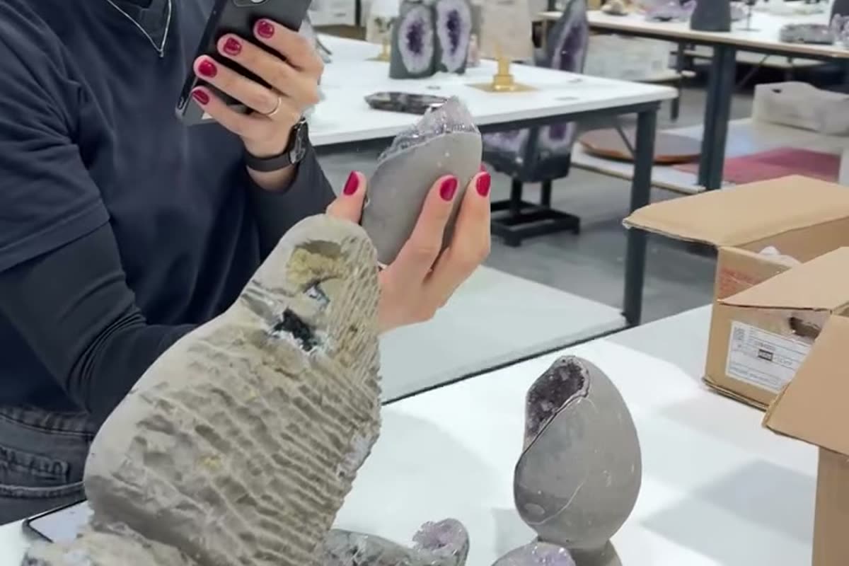 A CS Minerals seller broadcasting a live sale on a phone from the company warehouse in Brazil, holding an agate piece to the camera