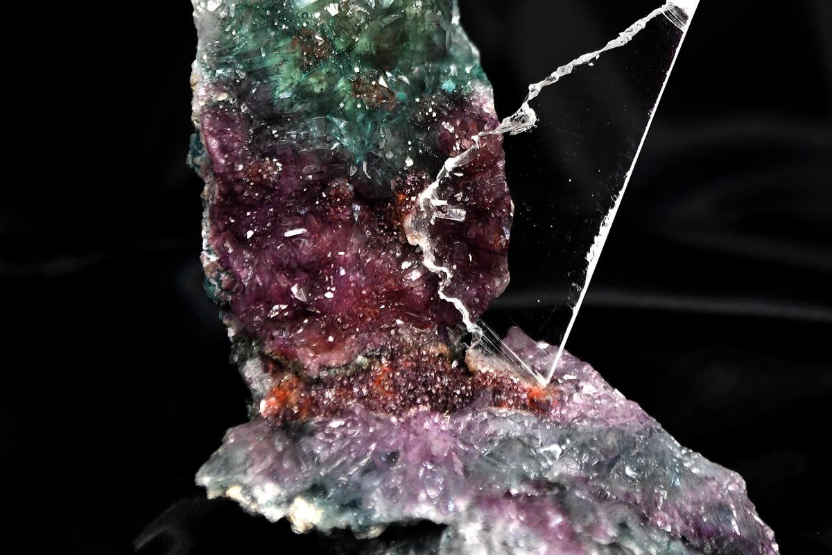 A premium Brazilian crystal specimen with green and deep purple faces, mounted on a clear acrylic display stand against a dark background