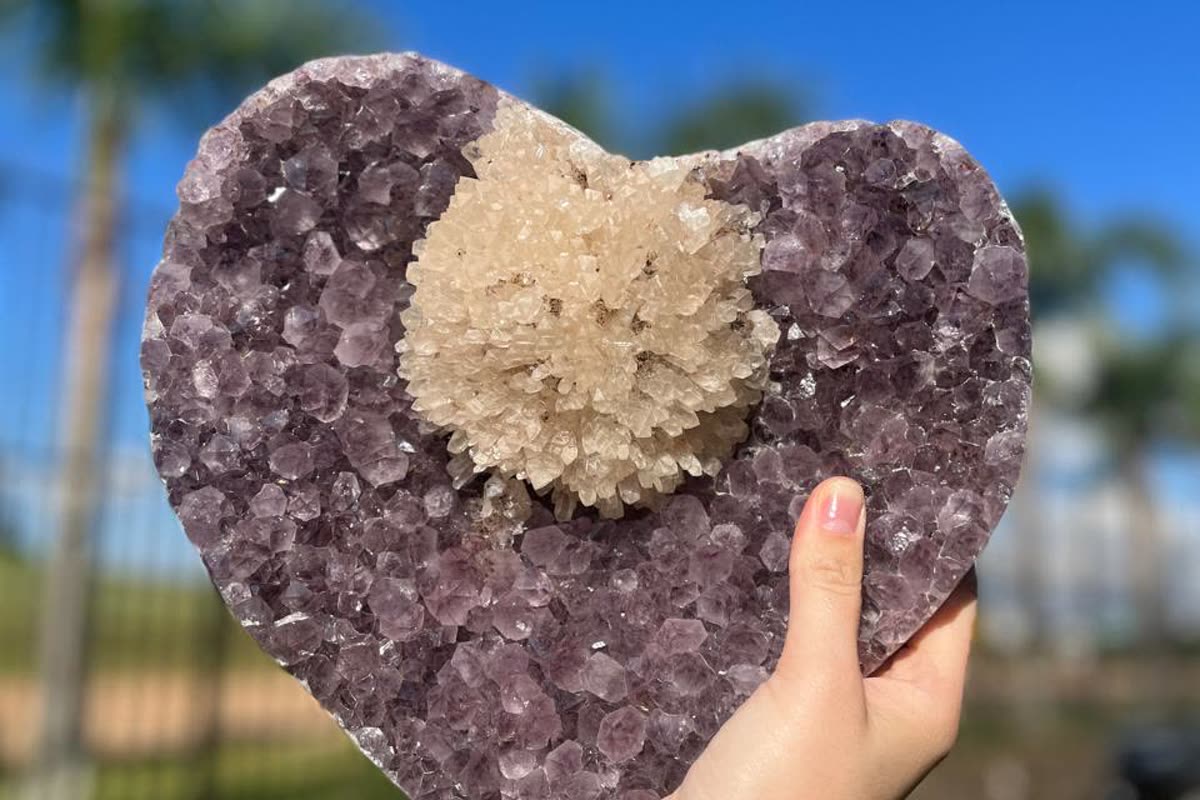 Large Brazilian amethyst heart with a calcite formation at its centre, held in one hand: a unique piece that wholesale crystals suppliers price individually