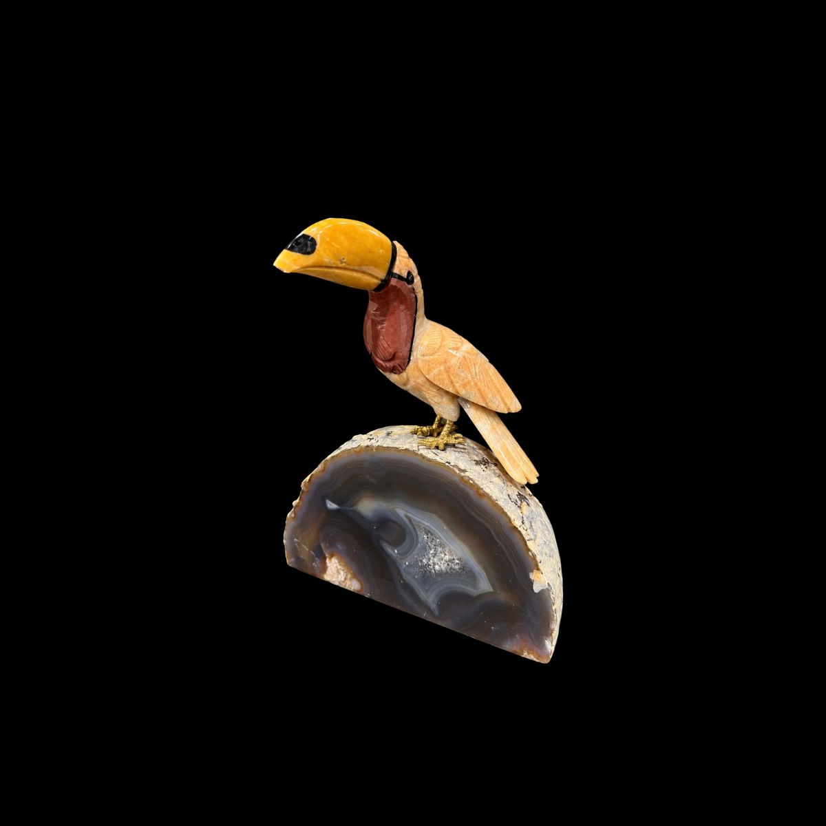 Carved stone toucan perched on a polished agate geode half, on a black background