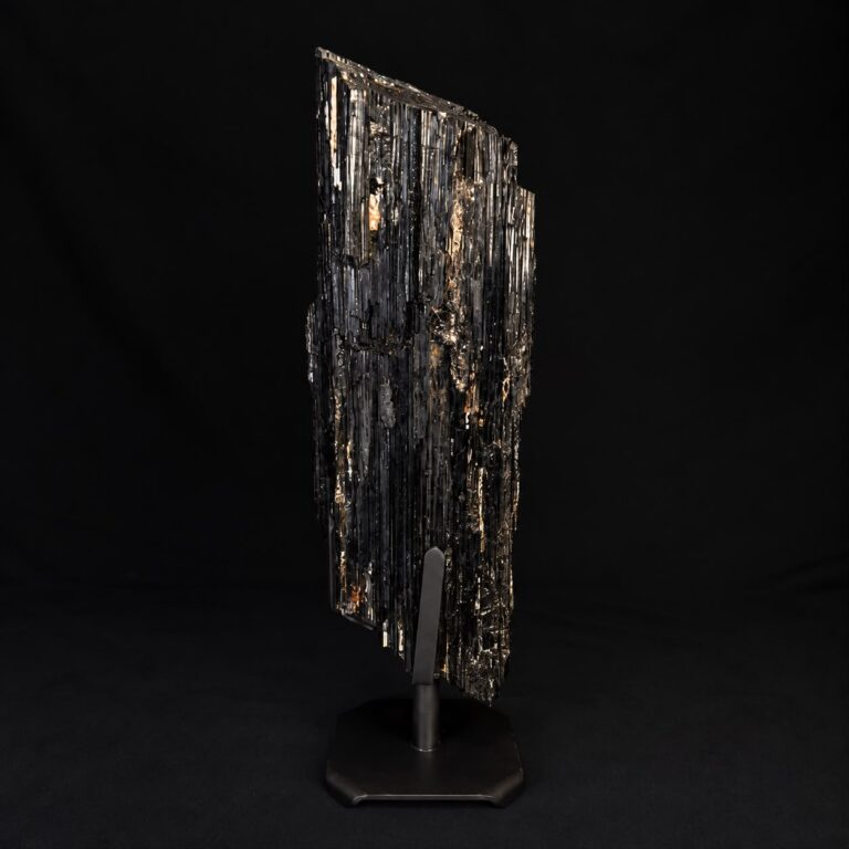 Dark mineral specimen on a display stand against a black background