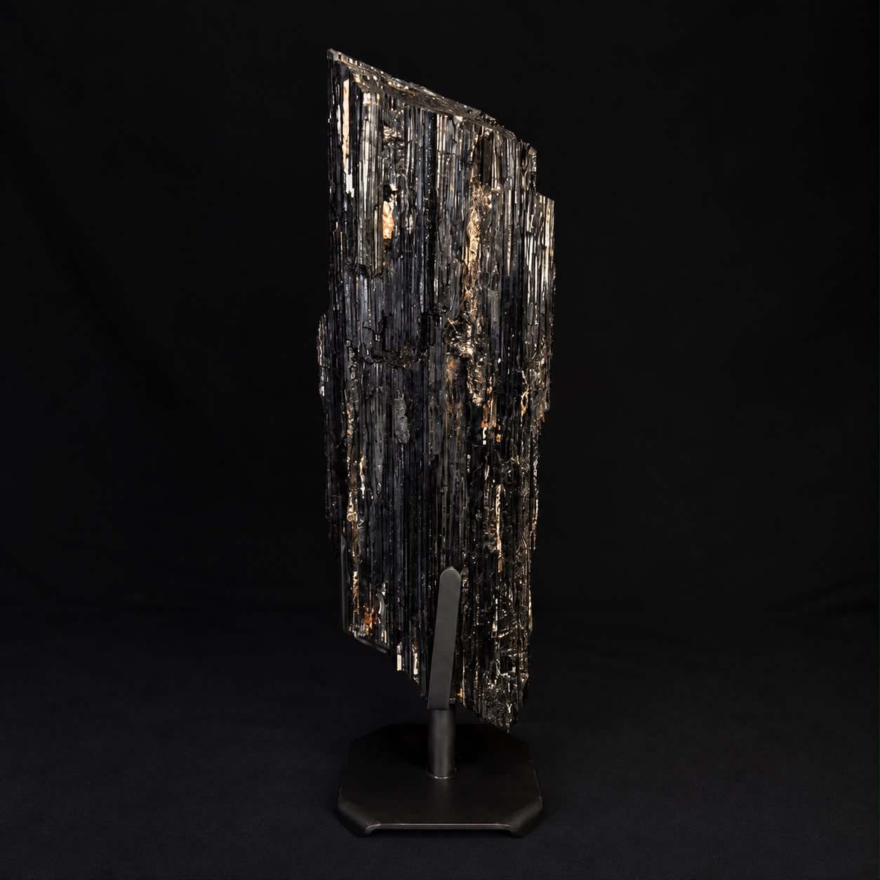 Dark mineral specimen on a display stand against a black background