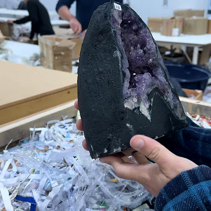 Hands holding an amethyst cathedral over shredded packing paper while the CS Minerals team packs crystal wholesale orders for buyers in Australia and worldwide