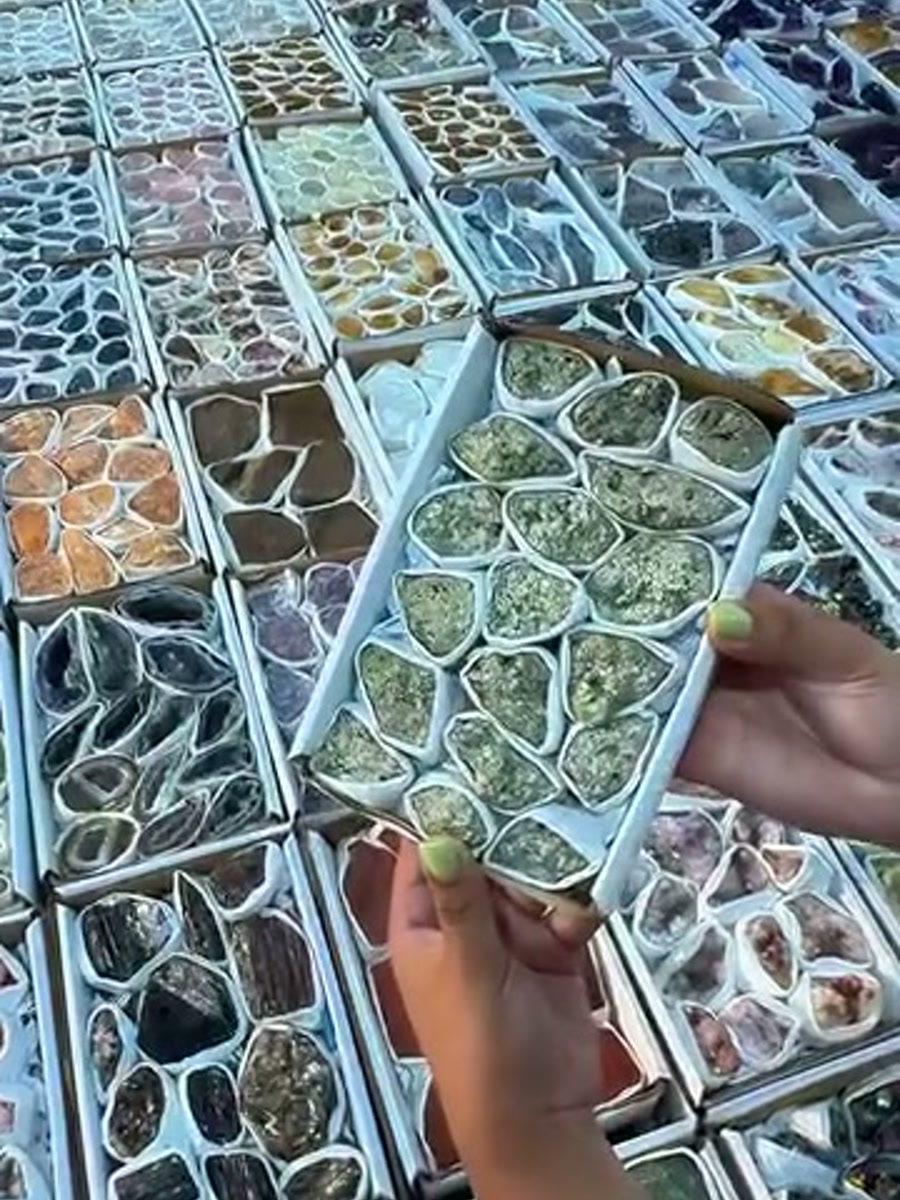 Sorted trays of tumbled Brazilian stones on a table at the CS Minerals warehouse, a hand lifting one tray, ready for crystal wholesale Netherlands orders