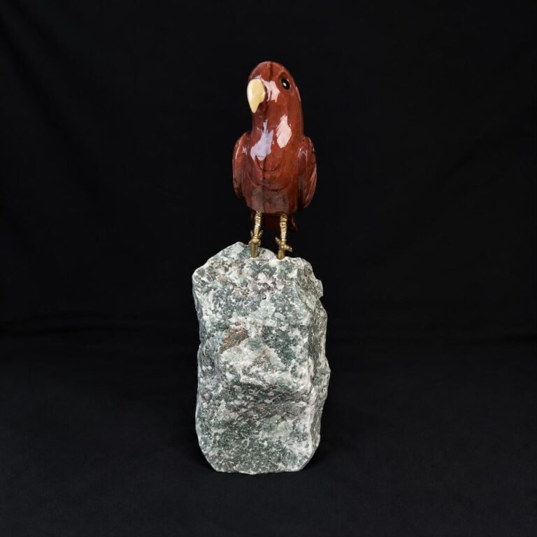 Polished red stone parrot carving perched on a rough green stone base